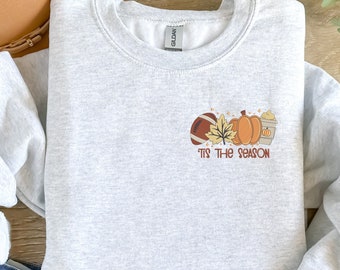 May include: A gray sweatshirt with a graphic of a football, a leaf, two pumpkins, and a cup of coffee. The text "Tis the season" is below the graphic.