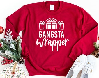 May include: Red Christmas sweatshirt with white text that says "Gangsta Wrapper" and a graphic of three wrapped presents with bows.