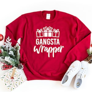 May include: Red Christmas sweatshirt with white text that says "Gangsta Wrapper" and a graphic of three wrapped presents with bows.