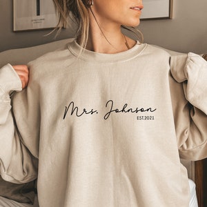 May include: A beige sweatshirt with the text "Mrs. Johnson EST. 2021" in black script.