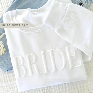 May include: White sweatshirt with the word "BRIDE" embroidered in raised white lettering.
