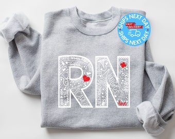 May include: Gray sweatshirt with a white design of the letters "RN" filled with medical-related words and symbols. The letters are outlined in white and have small red hearts inside them. The text "love" is written below the letters.