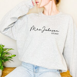 May include: Gray sweatshirt with the text "Mrs. Johnson EST. 2022" in black script font.