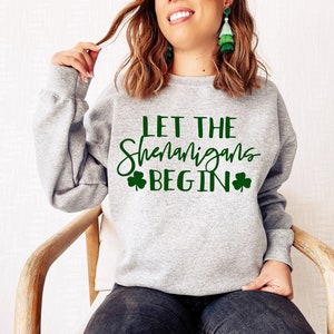 May include: Gray sweatshirt with the text "Let the Shenanigans Begin" in green lettering with shamrock symbols on either side of the text.