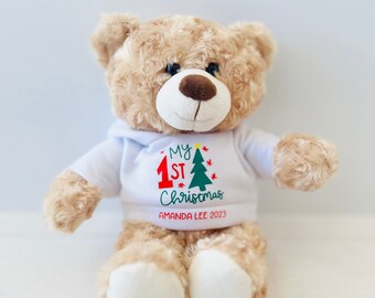 May include: A beige plush teddy bear wearing a white hoodie with the text "My 1st Christmas" and "Amanda Lee 2023" in red and green lettering.