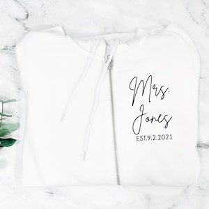 May include: White zippered hoodie with the text "Mrs. Jones EST. 9.2.2021" printed in black.