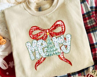Puede incluir: Sudadera beige con un diseño festivo. El diseño presenta la palabra "MERRY" en una fuente caprichosa, un árbol de Navidad y un gran lazo rojo. La sudadera está hecha de un material suave, perfecta para la temporada navideña.