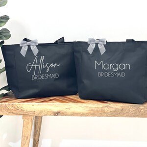 May include: Two black tote bags with gray ribbon bows. The bags are personalized with the names "Alison Bridesmaid" and "Morgan Bridesmaid".