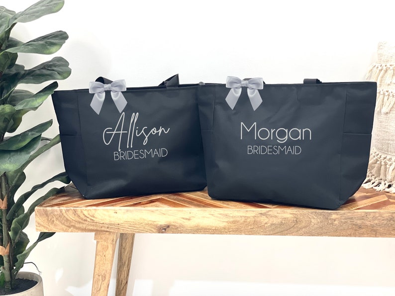 May include: Two black tote bags with gray ribbon bows. The bags are personalized with the names "Alison Bridesmaid" and "Morgan Bridesmaid".
