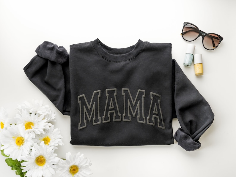May include: Black sweatshirt with the word "MAMA" in large, green, embroidered letters.