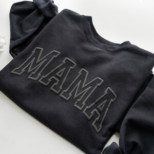 May include: Black sweatshirt with the word "MAMA" in raised, outlined lettering.