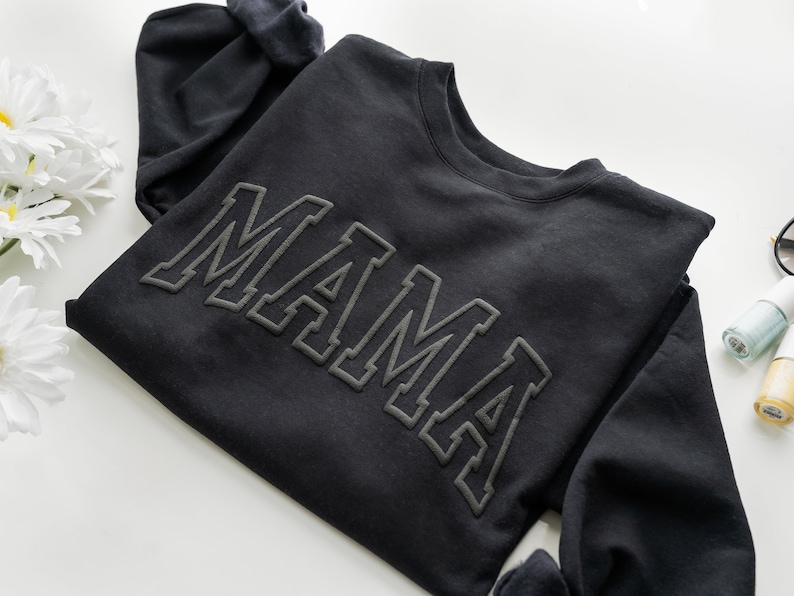 May include: Black sweatshirt with the word "MAMA" in raised, outlined lettering.