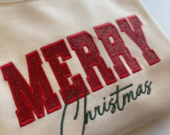 May include: A cream coloured sweatshirt with the word "MERRY" embroidered in red with a green outline. The word "Christmas" is embroidered in green cursive below the word "MERRY".