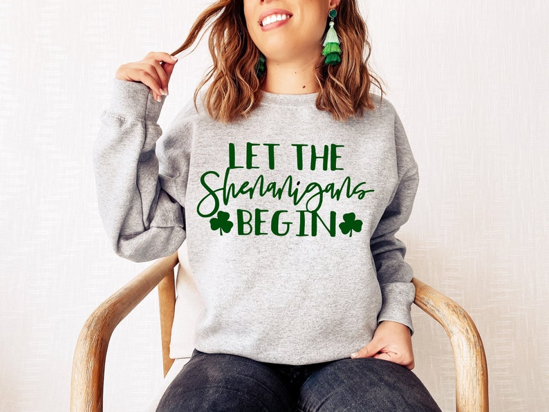 May include: Gray sweatshirt with the text "Let the Shenanigans Begin" in green lettering with shamrock symbols on either side of the text.