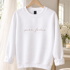 May include: A white long-sleeve crewneck sweatshirt featuring the word BRIDE embroidered in large white block letters across the chest, with the name mrs. fortes embroidered in a smaller, cursive gold script layered over the center.