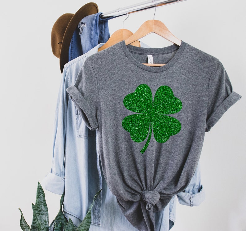 May include: A gray t-shirt with a green glitter four-leaf clover design.