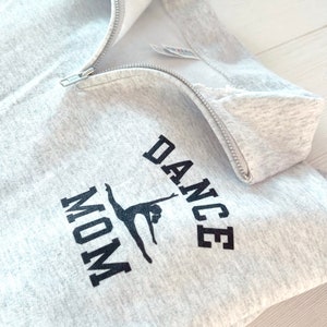 May include: Grey sweatshirt with a zip and the text "DANCE MOM" in black with a silhouette of a dancer in the middle.