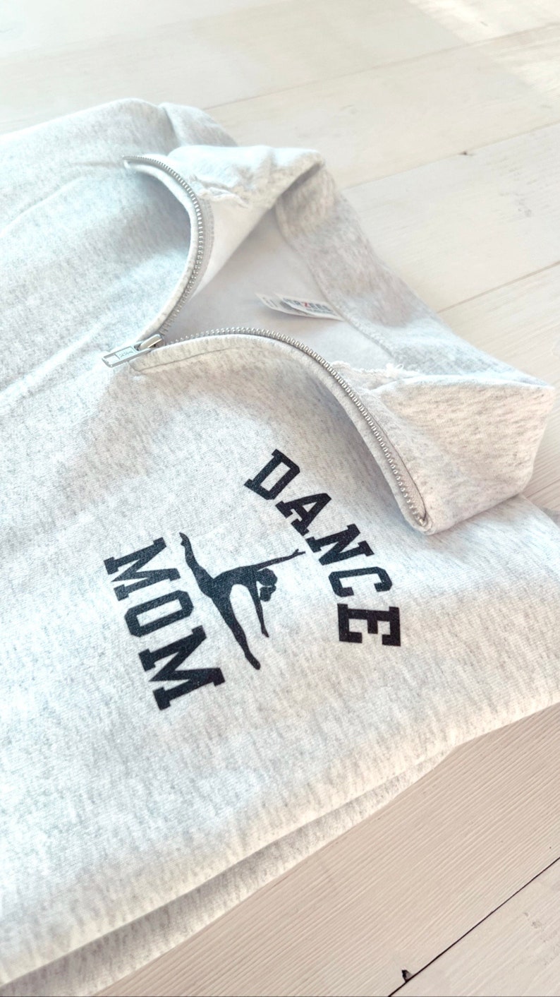 May include: Grey sweatshirt with a zip and the text "DANCE MOM" in black with a silhouette of a dancer in the middle.
