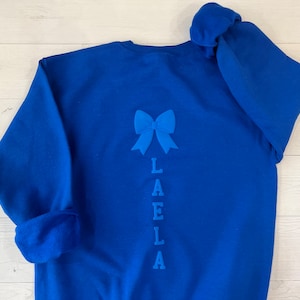 May include: Royal blue sweatshirt with a blue bow and the name "LAELLA" embroidered on the back.
