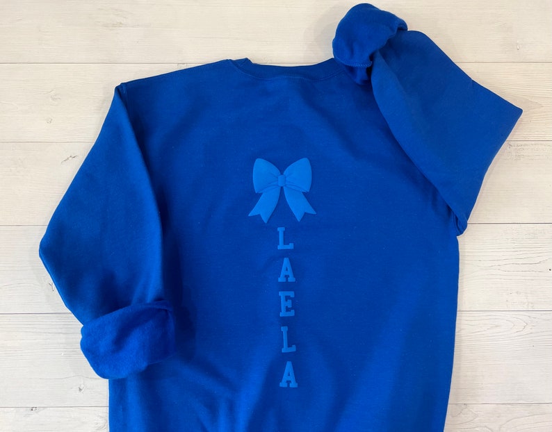 May include: Royal blue sweatshirt with a blue bow and the name "LAELLA" embroidered on the back.