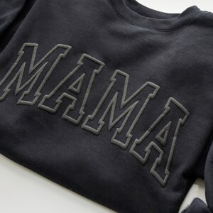 May include: Black sweatshirt with the word "MAMA" in large, outlined letters.