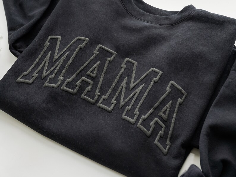 May include: Black sweatshirt with the word "MAMA" in large, outlined letters.