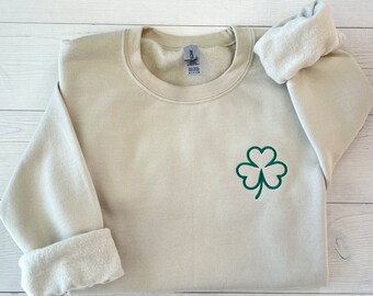 May include: A light beige sweatshirt with a green shamrock embroidered on the front.