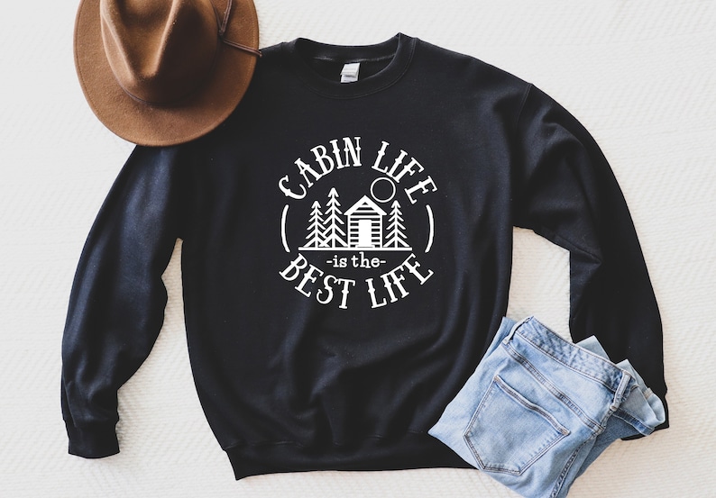 May include: Black sweatshirt with white text that reads "Cabin Life - is the - Best Life" with a graphic of a cabin and trees in a circle.