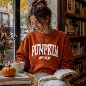 Op de afbeelding: Een roestoranje sweater met ronde hals en de witte tekst PUMPKIN SEASON in een collegiaal lettertype op de borst. Het kledingstuk met lange mouwen heeft een geribbelde halslijn, boorden en zoom voor een standaard pasvorm.
