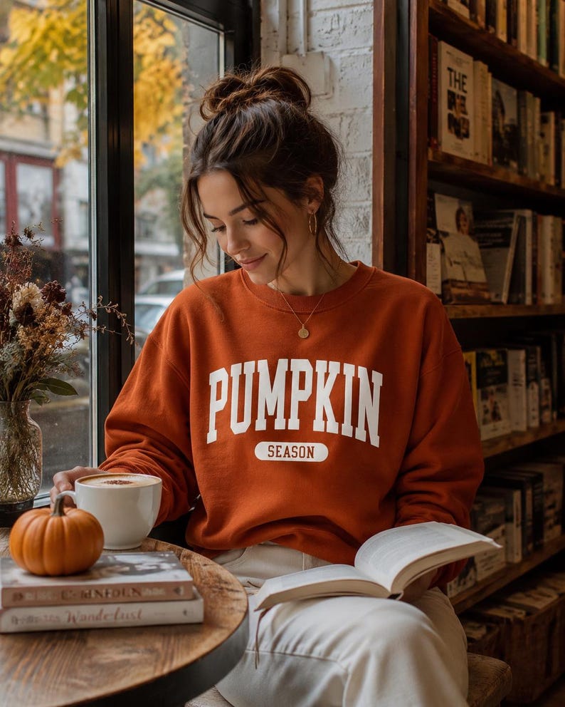Op de afbeelding: Een roestoranje sweater met ronde hals en de witte tekst PUMPKIN SEASON in een collegiaal lettertype op de borst. Het kledingstuk met lange mouwen heeft een geribbelde halslijn, boorden en zoom voor een standaard pasvorm.