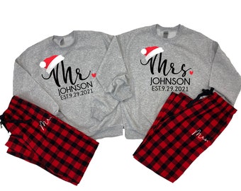 Könnte beinhalten: Passende graue Sweatshirts mit roten Weihnachtsmannmützen und dem Text "Mrs. Johnson Est. 9.29.2021" und "Mr. Johnson Est. 9.29.2021" darauf. Rot-schwarze karierte Schlafhosen mit dem Text "Mrs." und "Mr." darauf.