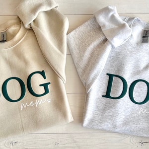 May include: Two sweatshirts, one beige and one gray, with the word "DOG" in dark green letters and the words "mom" in white letters below.
