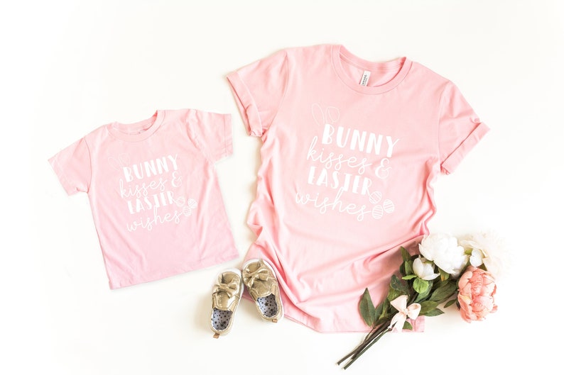 May include: Two pink t-shirts with the text "Bunny kisses & Easter wishes" in white. The smaller shirt is for a child and the larger shirt is for an adult.