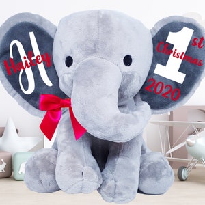 May include: A gray plush elephant with a red bow. The elephant's ears are personalized with the name "Hailey" and the text "1st Christmas 2020".