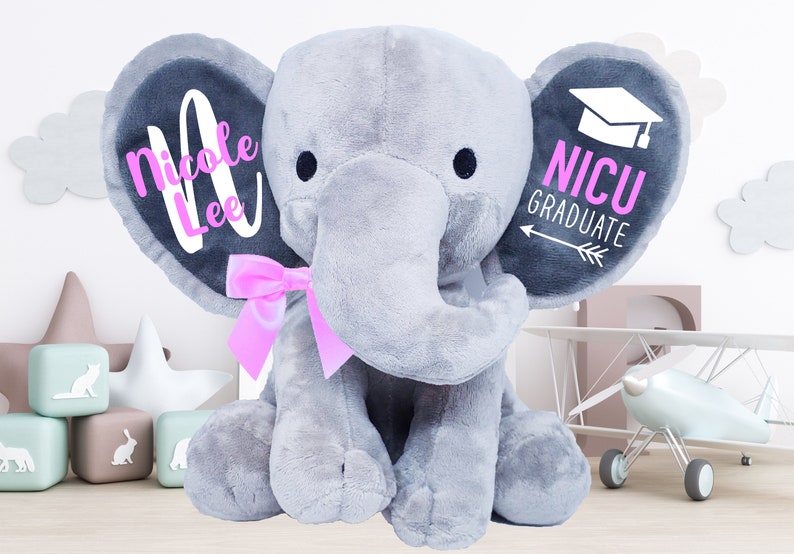 May include: Gray plush elephant with pink bow, personalized with the name "Nicole Lee" on one ear and "NICU GRADUATE" with a graduation cap on the other ear.