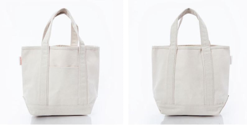 May include: A cream-colored canvas tote bag featuring two sturdy top handles, a flat base, and a single exterior slip pocket on the front. The bag is constructed from a durable woven fabric with reinforced stitching along the handles and seams.