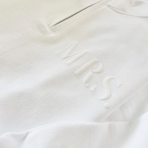 Op de afbeelding: Witte hoodie met rits en het woord "MRS." geborduurd op de voorkant.