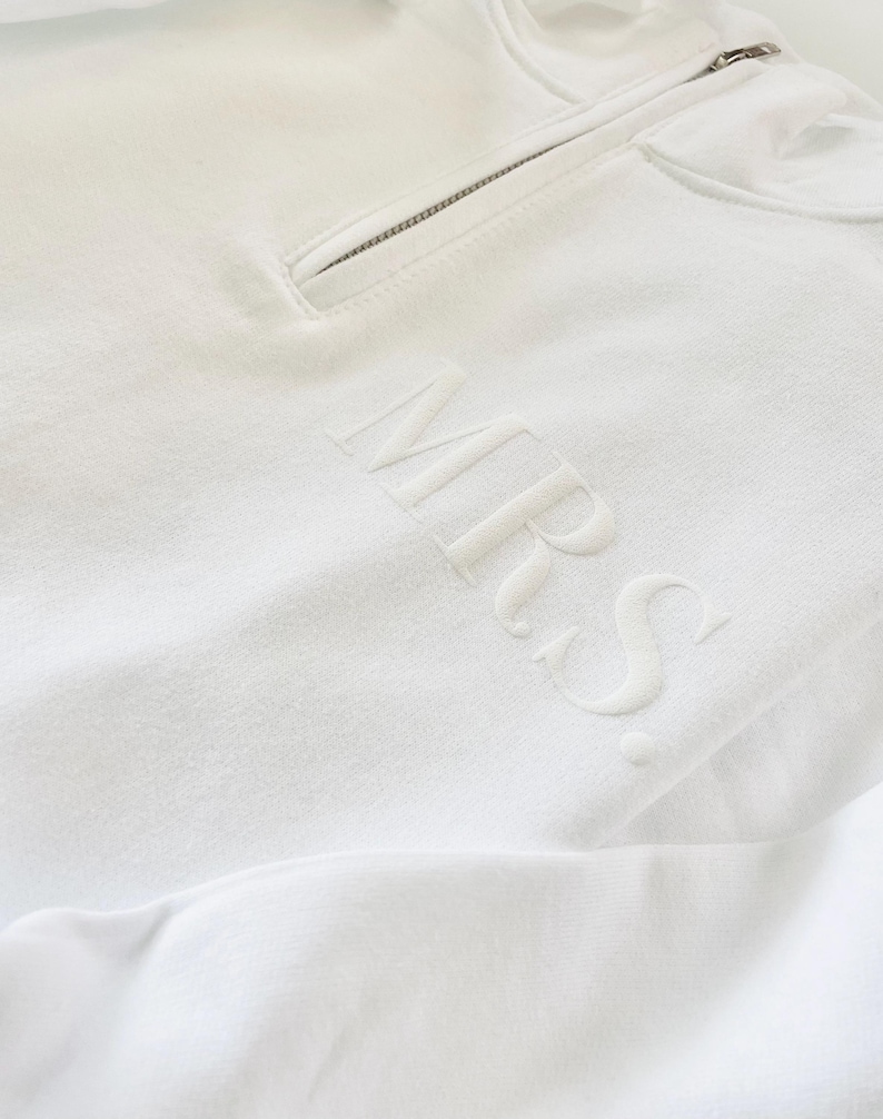 Op de afbeelding: Witte hoodie met rits en het woord "MRS." geborduurd op de voorkant.