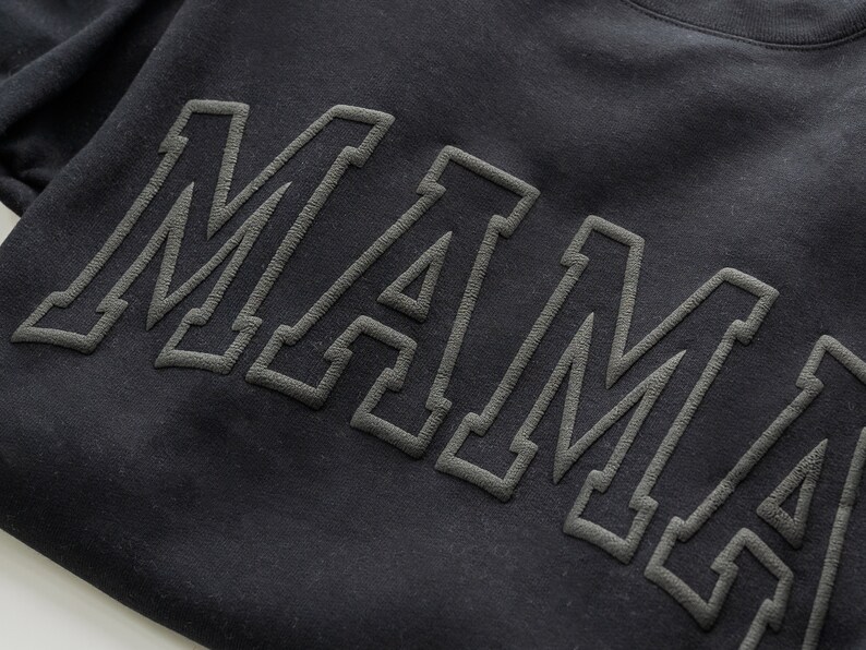 May include: Black sweatshirt with the word "MAMA" in large, outlined letters.