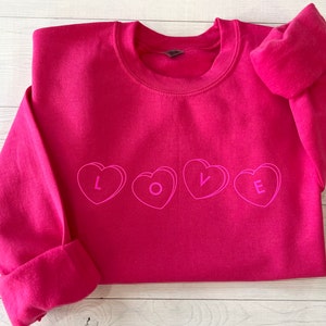 May include: A pink sweatshirt with the word "LOVE" spelled out in white outlined hearts.
