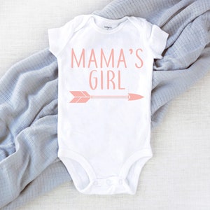 Pu&ograve; includere: Body bianco per neonato con testo rosa che recita "Mama's Girl" e una freccia rosa.