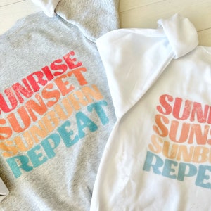 May include: Two sweatshirts with the text "Sunrise Sunset Sunburn Repeat" printed on the back. The sweatshirts are in grey and white.