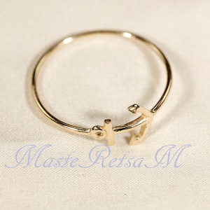 May include: A gold-toned ring with an anchor design. The anchor is a simple, stylized design.
