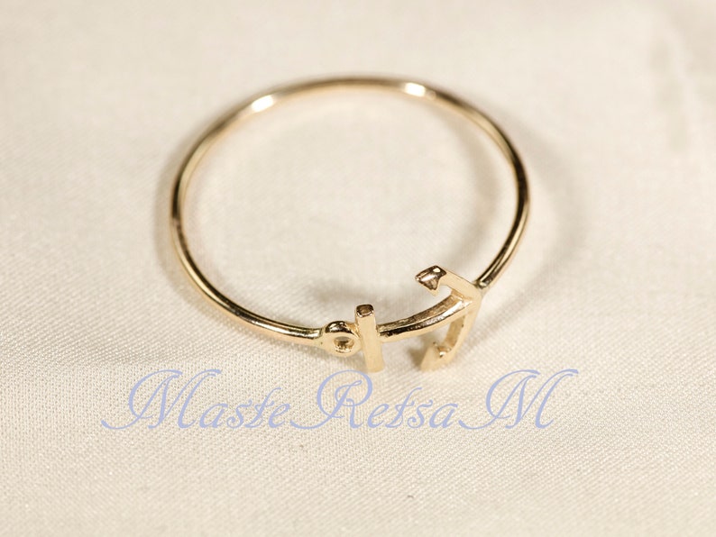 May include: A gold-toned ring with an anchor design. The anchor is a simple, stylized design.