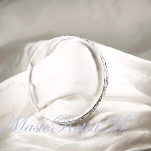 May include: A silver bangle bracelet with a delicate, intricate design. The bracelet is smooth and shiny, and it appears to be made of high-quality metal.