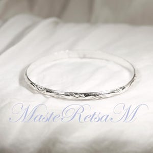 May include: A silver bangle bracelet with a twisted design. The bracelet is on a white fabric background.