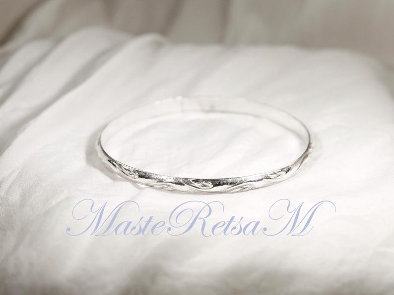May include: A silver bangle bracelet with a twisted design. The bracelet is on a white fabric background.