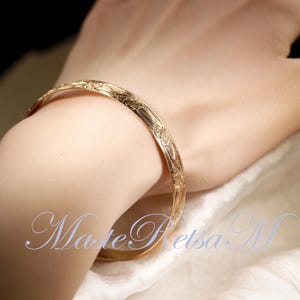 May include: A gold bangle bracelet with an intricate floral design.