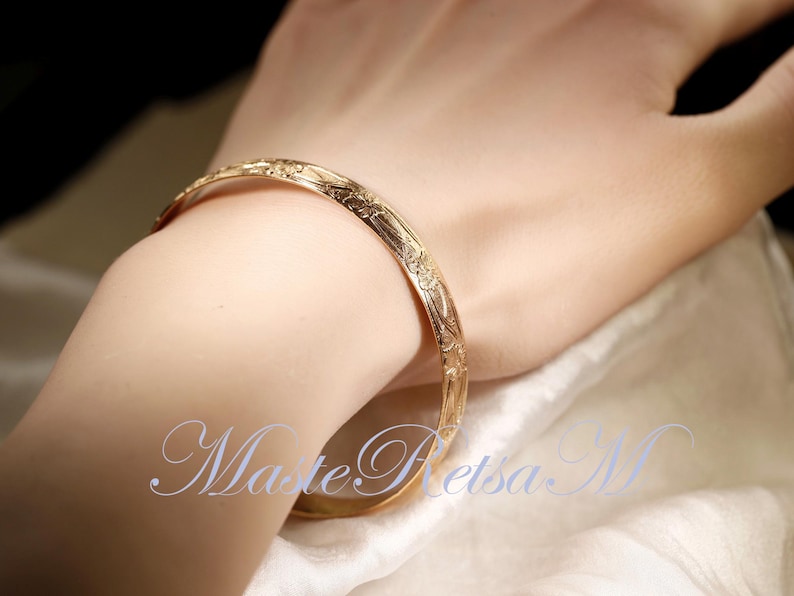 May include: A gold bangle bracelet with an intricate floral design.