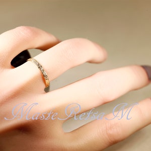 Puede incluir: Un fino anillo de banda de oro con un dise&ntilde;o texturizado. El anillo se lleva en un dedo con esmalte de u&ntilde;as marr&oacute;n claro.
